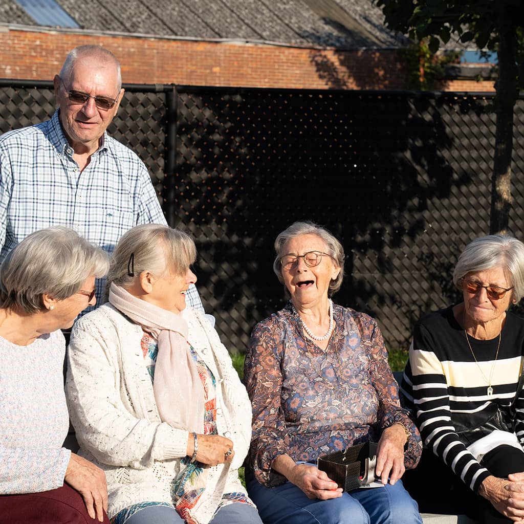 Bewoners zitten op een bank en lachen samen in de tuin van Gaudium assistentiewoningen in Mol